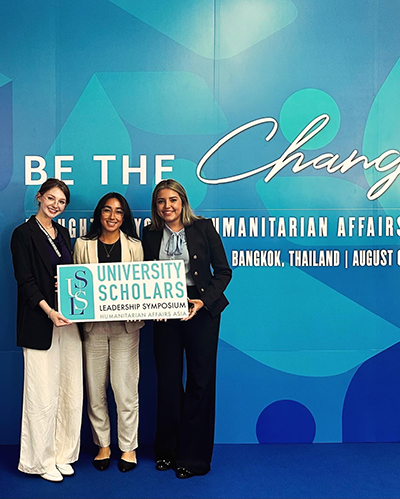 Three students in front of a sign that says "Be the Change"